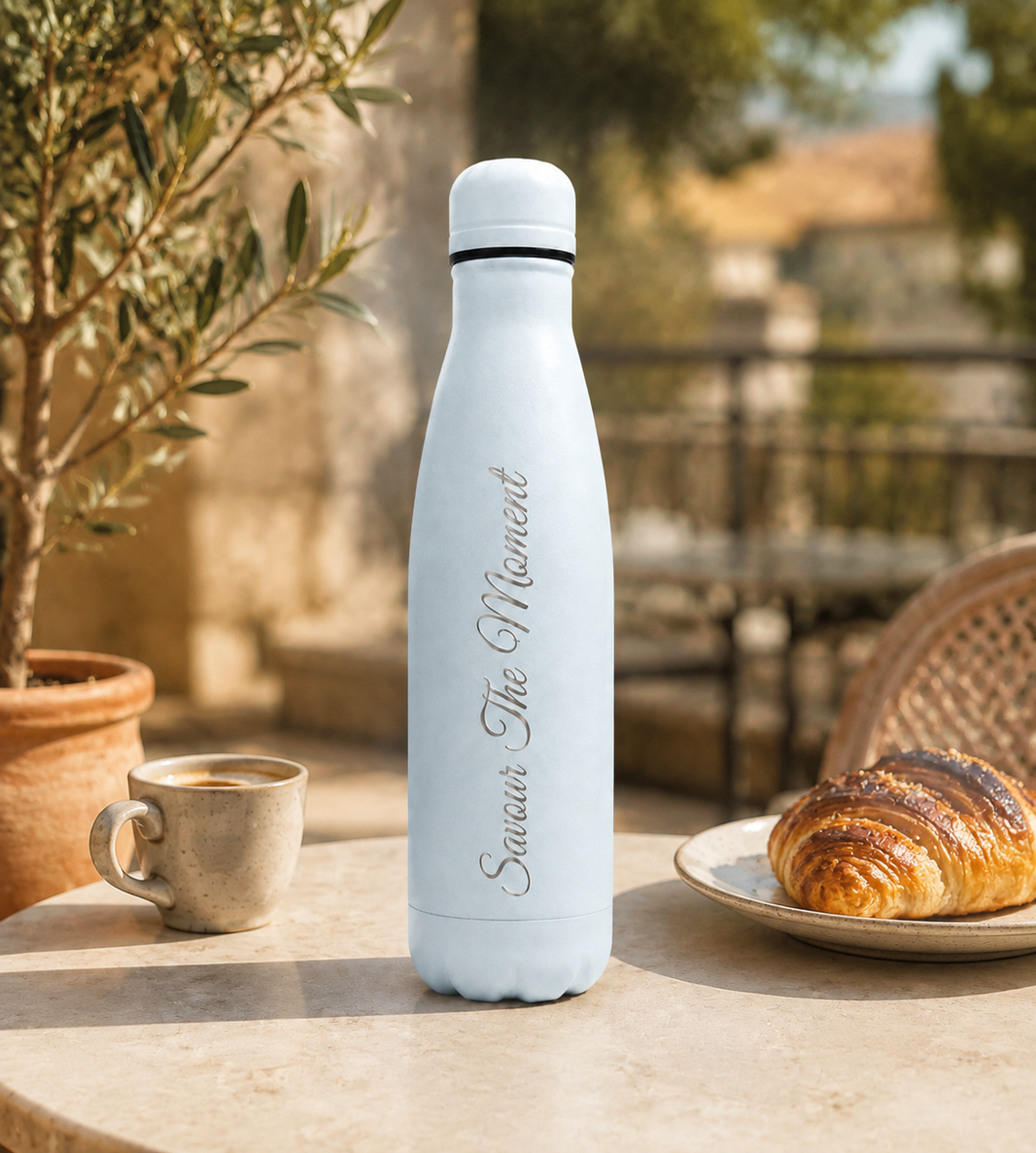 Sky Blue personalised stainless steel water bottle engraved “Savour The Moment” beside coffee and a croissant on a sunlit café breakfast table