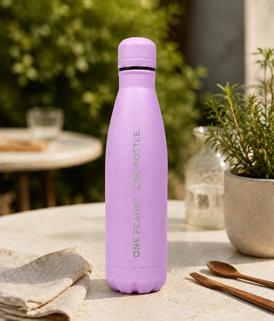 Light purple personalised stainless steel cola-shaped water bottle engraved “One Planet, One Bottle” on an outdoor garden table.