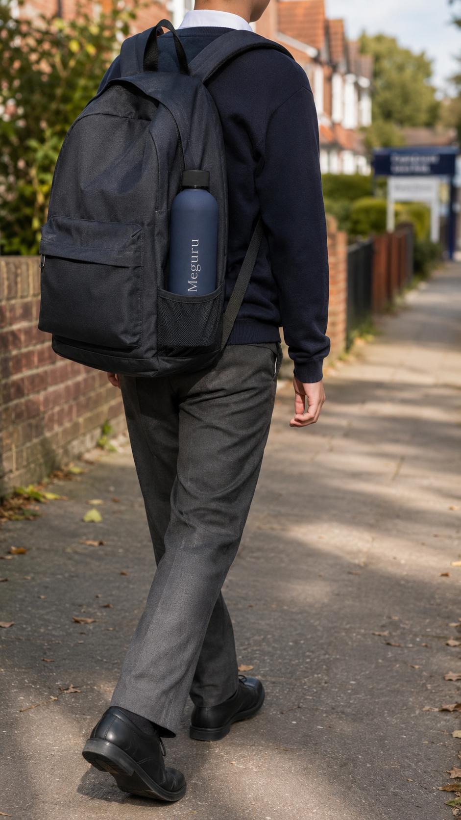 Navy blue personalised stainless steel water bottle engraved “Meguru” in a school backpack as a student walks to school.