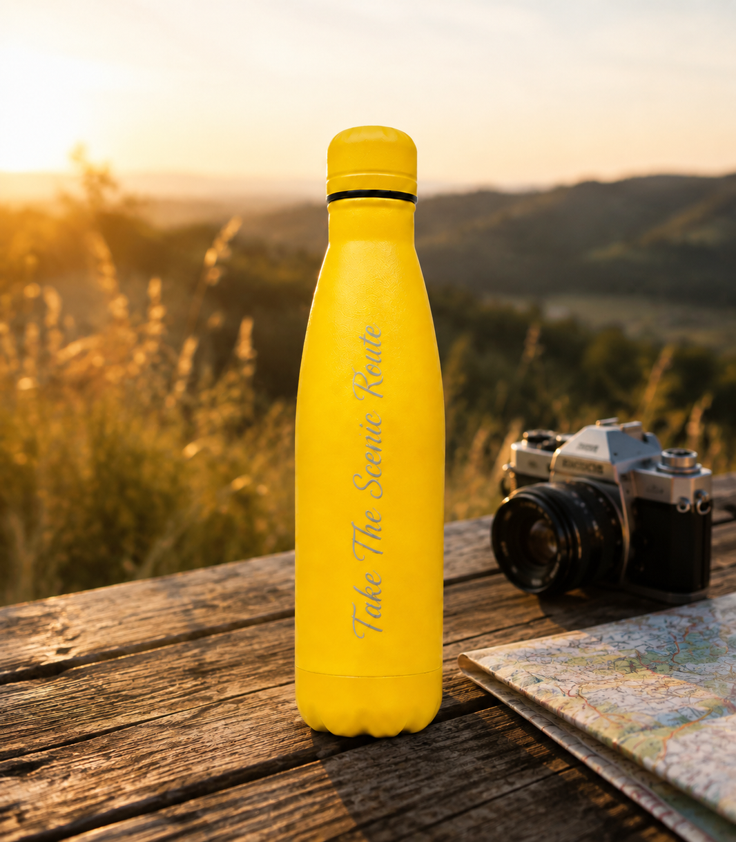 Yellow 500ml personalised stainless steel water bottle engraved “Take The Scenic Route” on an outdoor travel table at sunset with camera and map | Willys Bottles
